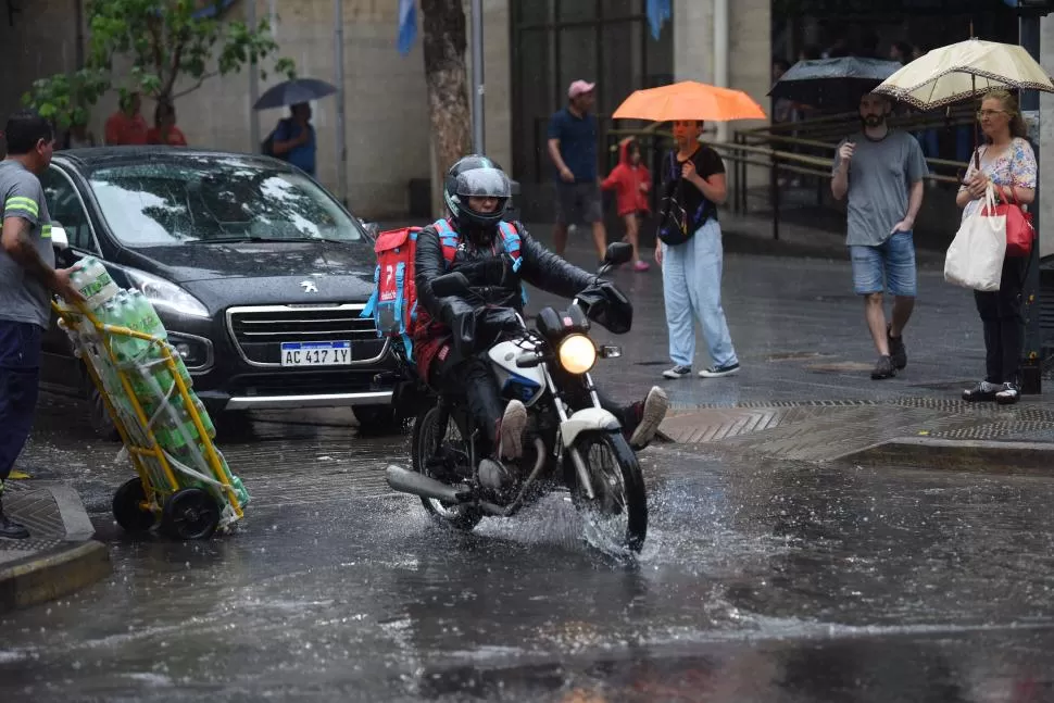 DE VEREDA A VEREDA. Un repartidor de comida intenta no mojarse más de lo inevitable en su recorrido.
