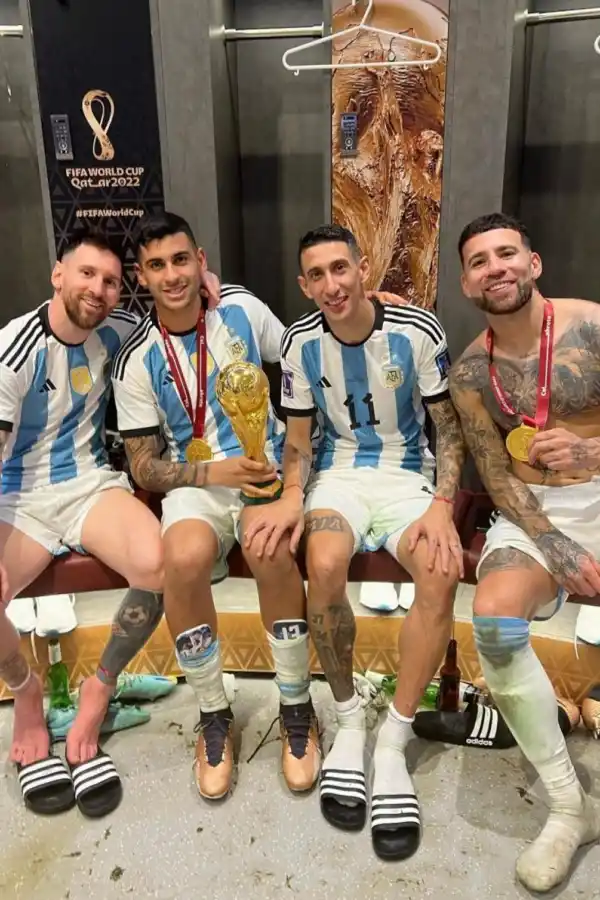 EN EL VESTUARIO. Lionel Messi, Cristian Romero, Ángel Di María y Nicolás Otamendi lucen el trofeo, que no conservarán, pero sí las medallas que serán el recuerdo que podrán tener en sus vitrinas.  
