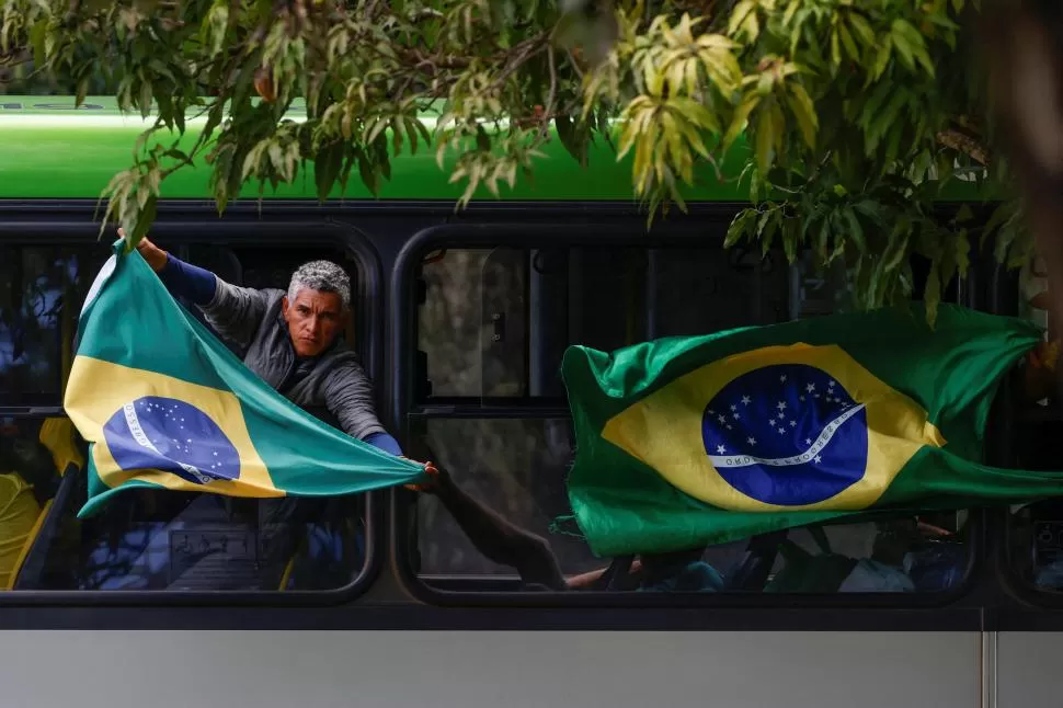 PROVOCACIÓN. Un bolsonarista despliega una bandera de Brasil desde un ómnibus de la Academia de la Policía federal tomado por manifestantes. fotos REUTERS