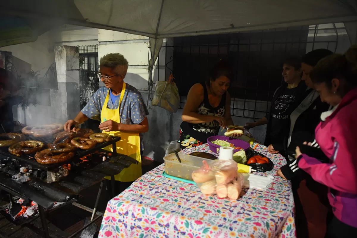 ENFOCADA EN LO SUYO. Sobre calle Bolívar, Norma Ponce cocina los chorizos en la previa del partido, mientras sus hijos y nietos colaboran con la preparación. 