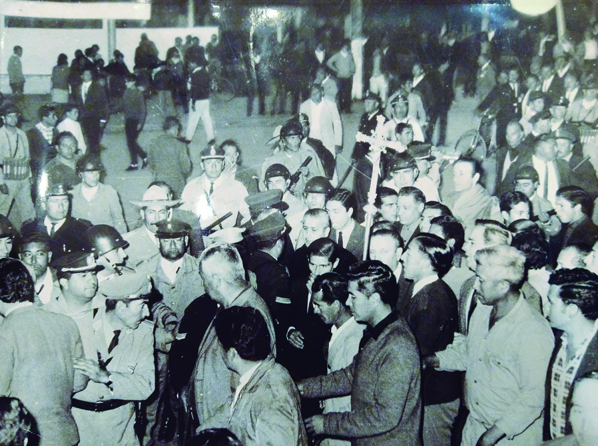 La foto es una postal del inicio de la década del 70, tiempo de luchas sociales en Tucumán. La Policía interrumpe la marcha de una procesión. Al centro, al cobijo de la cruz, se ve a Dip hablando con un agente.