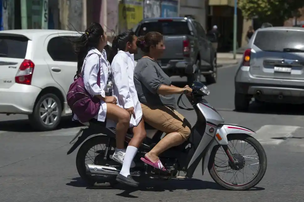 DE A TRES. Una madre traslada a dos alumnas en moto y sin casco.