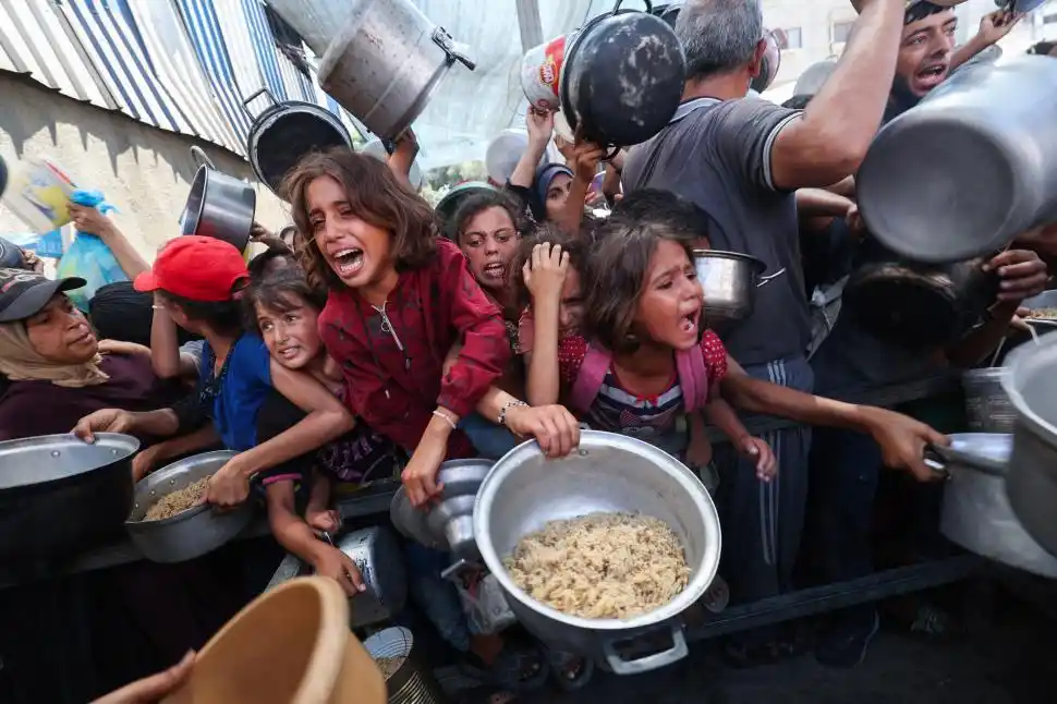 HAMBRE. Niños palestinos, a los empujones, tratan de conseguir una comida caliente en el campo de Nuseirat.  