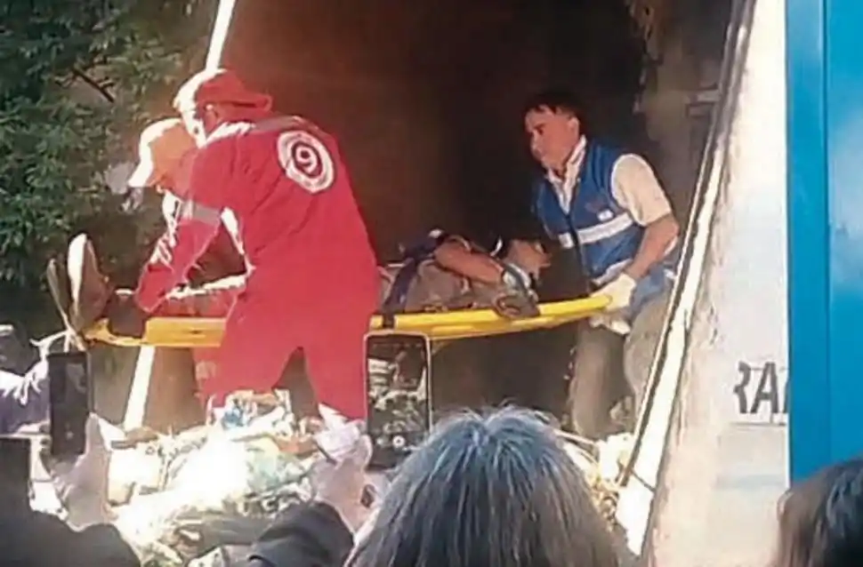 EL HORROR. El instante en que rescatan a un joven del interior de la compactadora del camión de residuos.