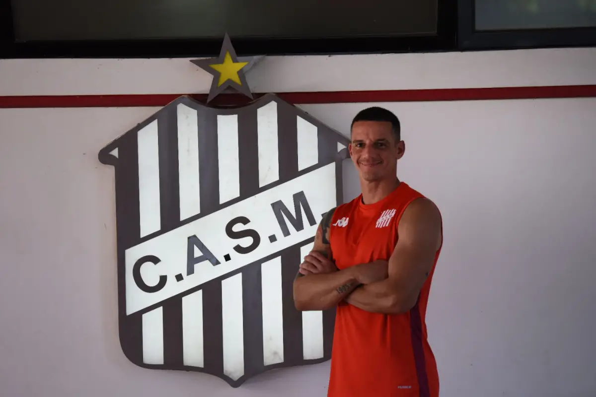 SONRÍE Y SIGUE. Darío Sand posa frente al escudo de San Martín tras confirmar su continuidad y renovar la ilusión para la temporada 2026.