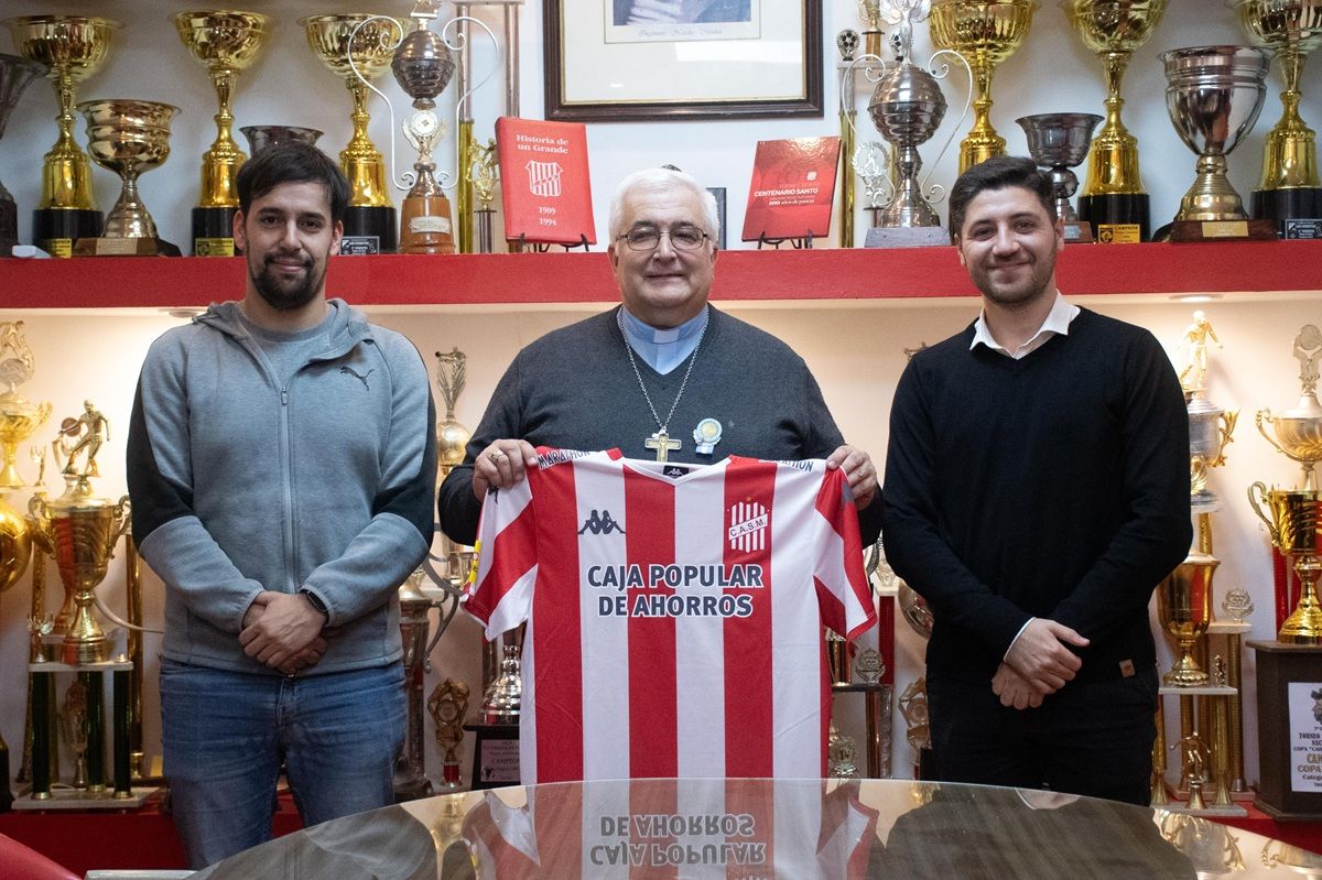 CON LA DEL SANTO. El arzobispo sostiene la camiseta titular de San Martín junto al vicepresidente Nicolás Nasrallah (derecha) y el prosecretario Gerónimo García Mirkin.