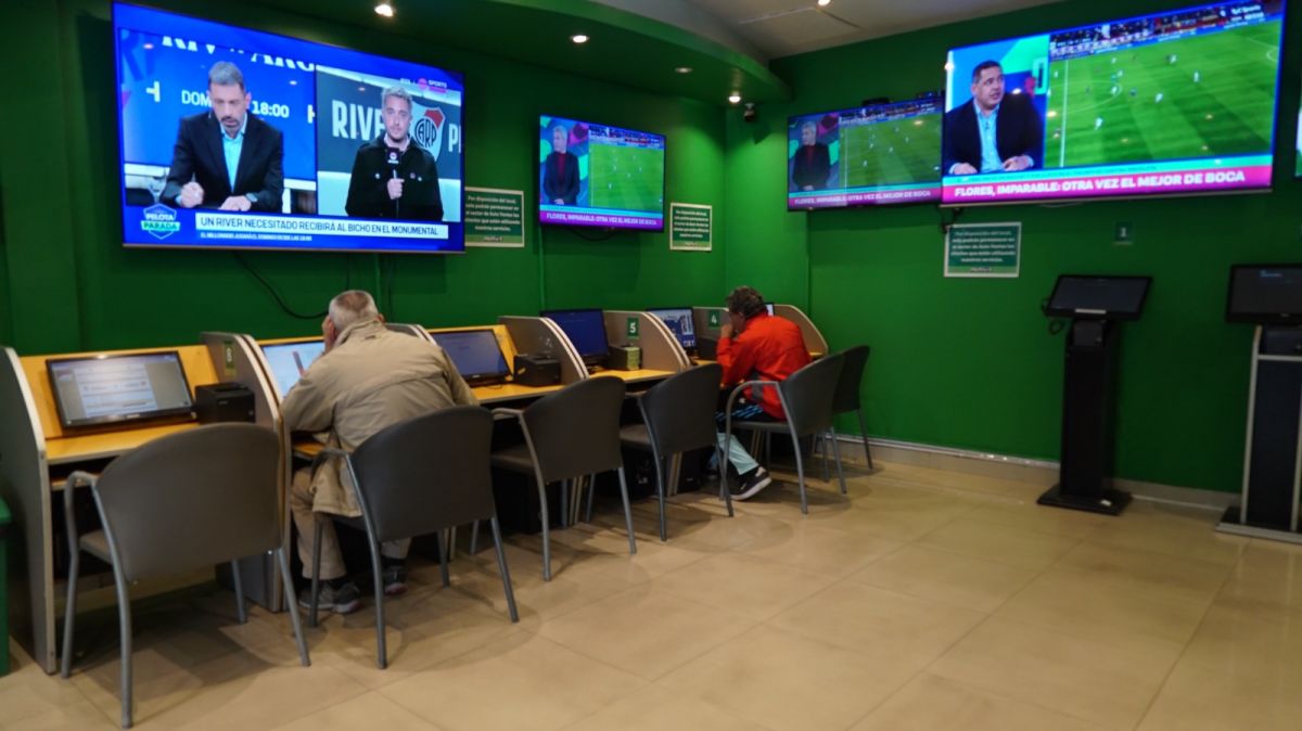 ESCENA. El interior de un local de Pálpitos, con clientes frente a las terminales y televisores que transmiten distintos eventos deportivos.