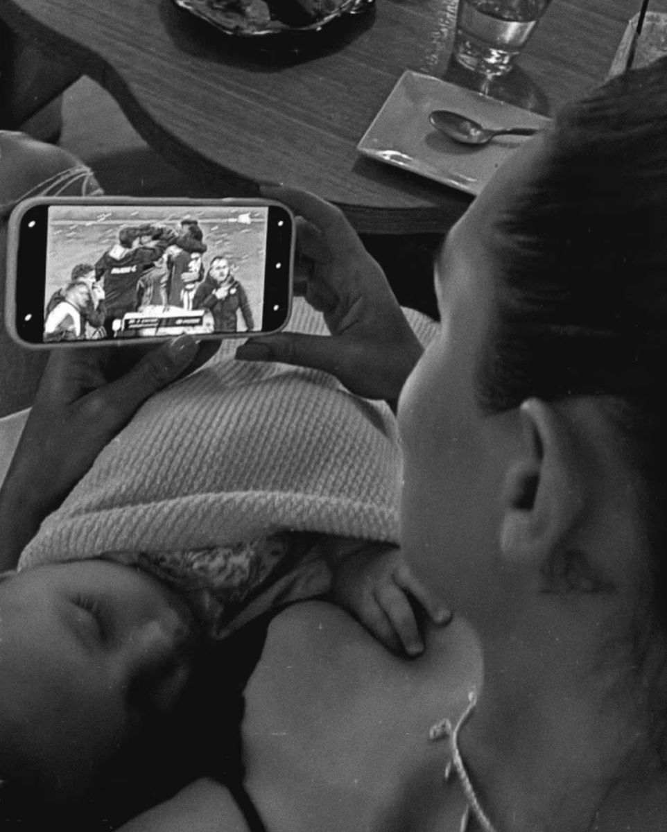 Cami Homs observa en un teléfono móvil el partido de Estudiantes de La Plata mientras sostiene a su hija Aitana durante su estancia en Estados Unidos